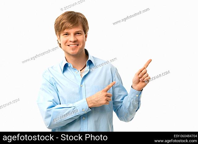 Happy young man pointing to blank space on the right, smiling. Copyspace, isolated on white