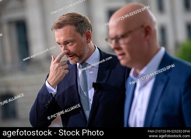 25 July 2021, Berlin: Christian Lindner (l), party leader of the FDP, holds his nose before the ARD summer interview on the terrace of the...