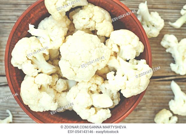 Cauliflower in a clay bowl on a wooden table, top view, rustic style