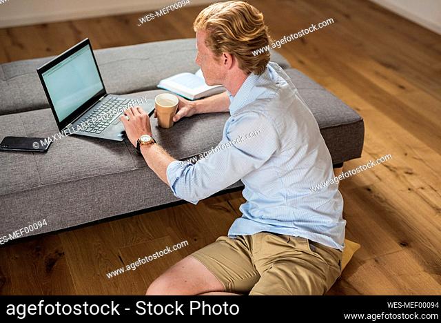 Businessman working on laptop with coffee cup in living room