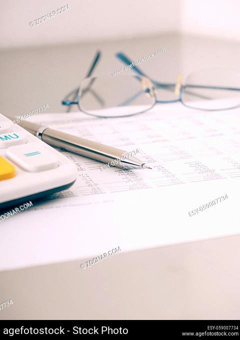 A close-up shot of a calculator. A printed balance sheet and a pen are also visible