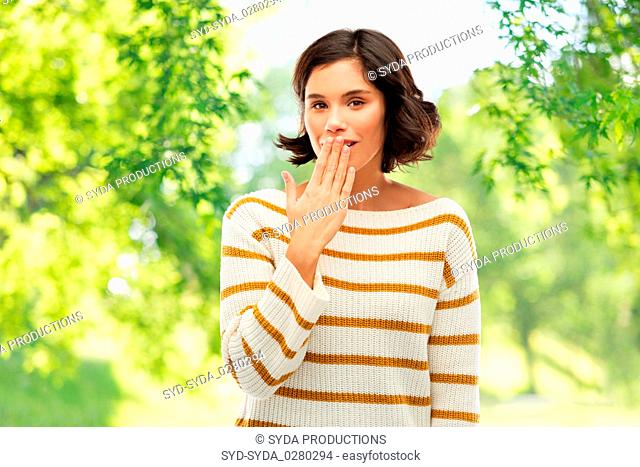 woman covers mouth by hand over natural background
