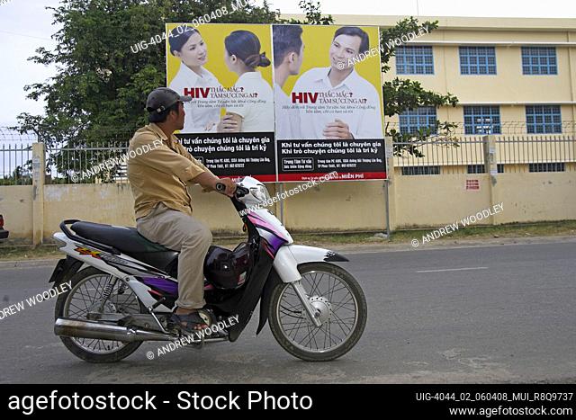 Man on motorcycle pauses to look at roadside HIV posters Phan Thiet south east Vietnam