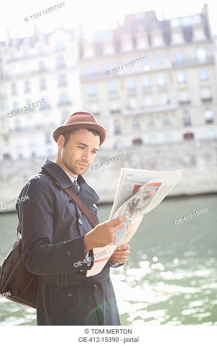 Businessman reading newspaper along Seine River, Paris, France