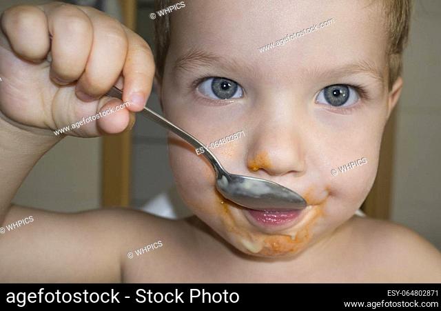 Baby boy eating by himself with spoon. Closeup