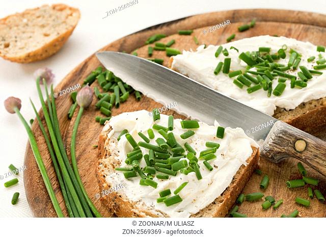 whole grain bread slices with cream cheese, green chopped chives. peeper and salt on a wood cutting board