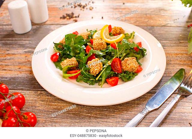 fresh salad of cherry tomatoes, croutons and capelin roe, mixed lettuce leaves in a white dish on an old wooden table, top view