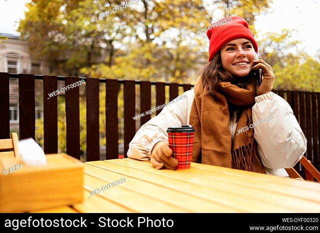 Young woman smiling while talking on mobile phone sitting at sidewalk cafe