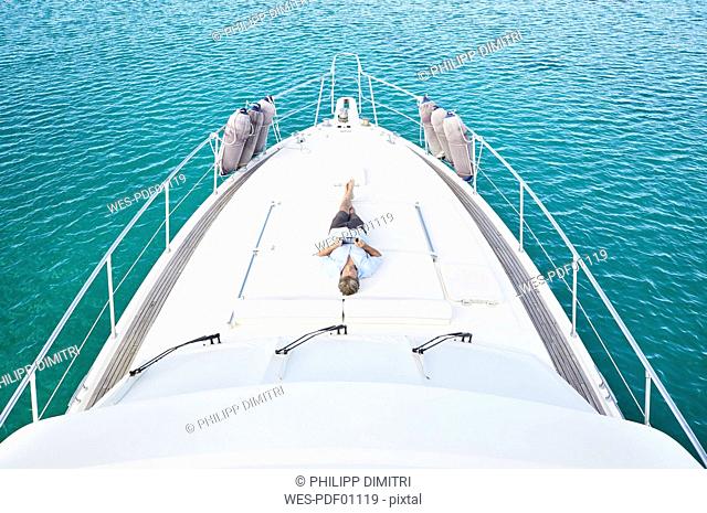Smiling man lying on deck of his motor yacht using tablet