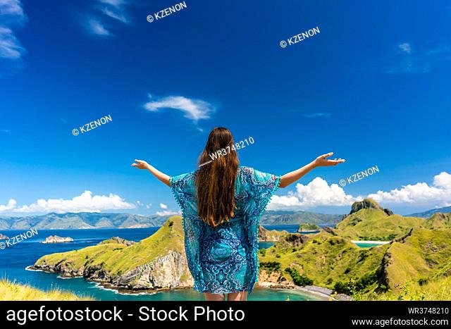 Rear view of a happy tourist enjoying the breeze while standing with outstretched arms outdoors during summer vacation in Padar Island, Indonesia