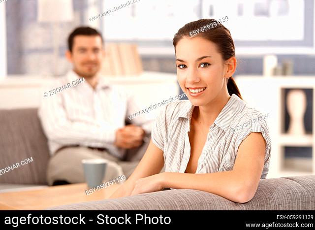 Young couple sitting in living room on sofa, smiling