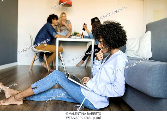 Woman sitting on floor using laptop with friends in background