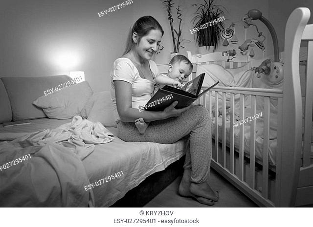 Black and white image of young mother reading book to her baby son before going to bed