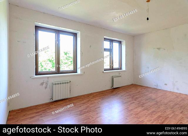 The interior of an empty room during renovation, there are two large windows in the room, radiators under them