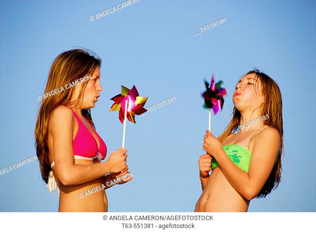 girl 13, girl 18 yrs blowing on pinwheels at beach
