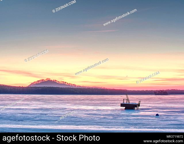 Low light orange and blue at lake under ice. Frozen beach sand, blue sky and orange sun at sunset. Beautiful natural scenery