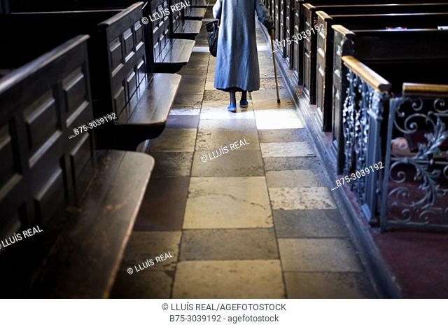 Unrecognizable old lady walking for the corridor of a church. London, England
