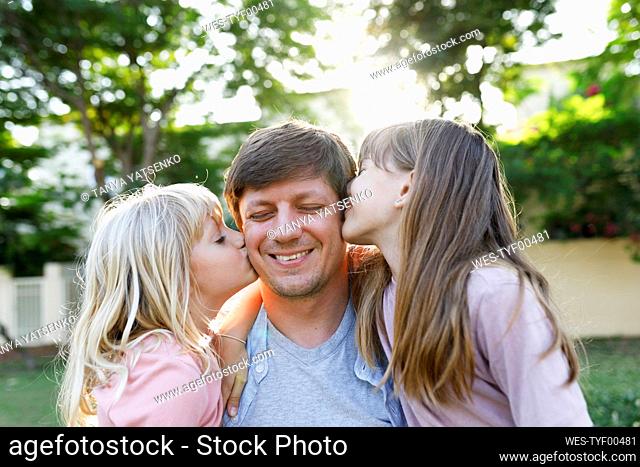 Smiling father with daughters kissing him on cheek at park
