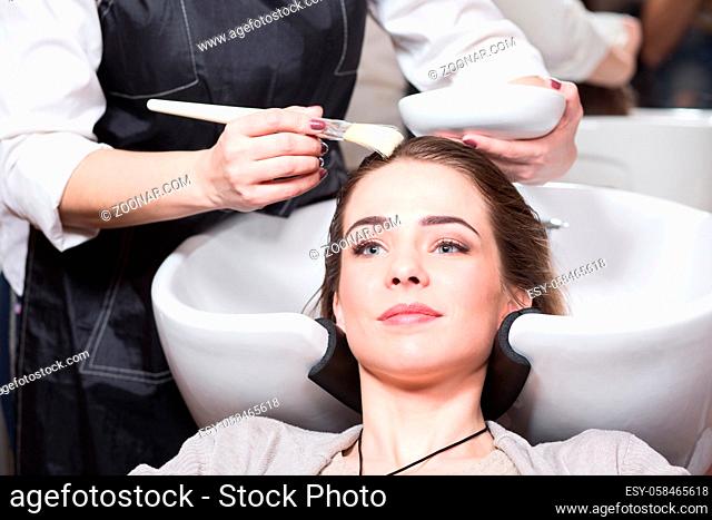 Beautiful lady having her hair washed by hairdresser in hairdressing saloon. Barber girl combing her hair in beauty saloon