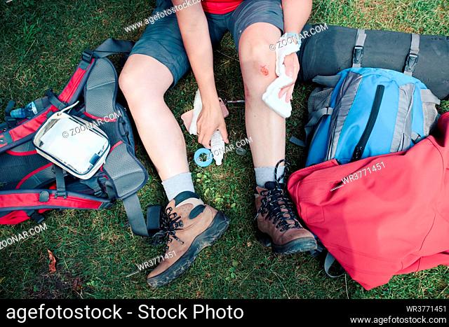 Woman injured in the accident on mountain hike. Dressing the wound on her knee with medicine in spray and gauze sitting on grass