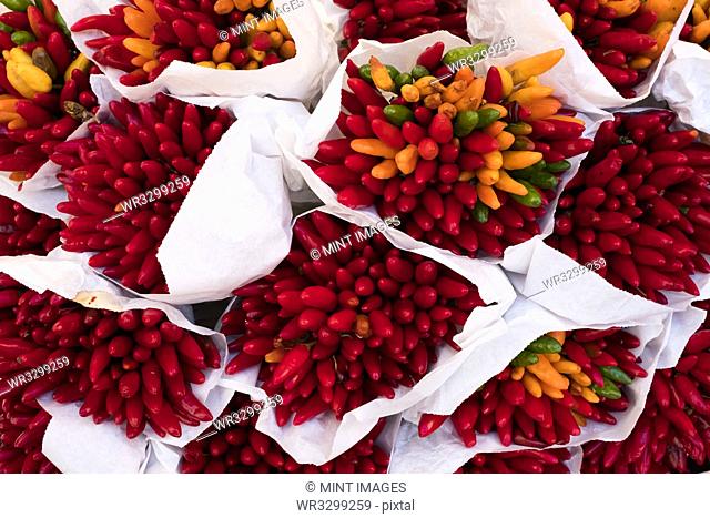 High angle close up of a large bunches of fresh red and orange chillies at a market stall
