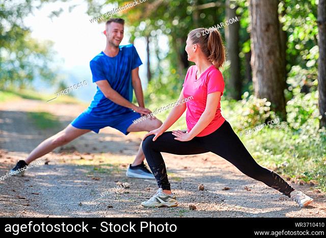 young happy couple enjoying in a healthy lifestyle warming up and stretching before jogging on a country road through the beautiful sunny forest
