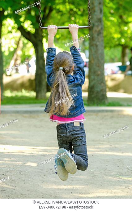 A girl is riding a metal ladder on chains in a playground
