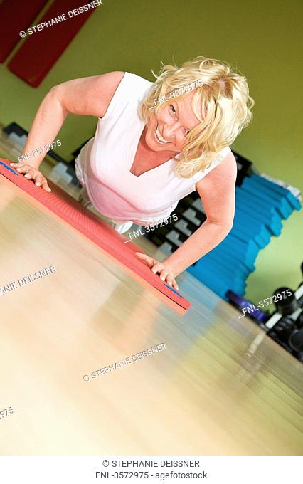 Mature woman exercising on gymnastics mat in gym