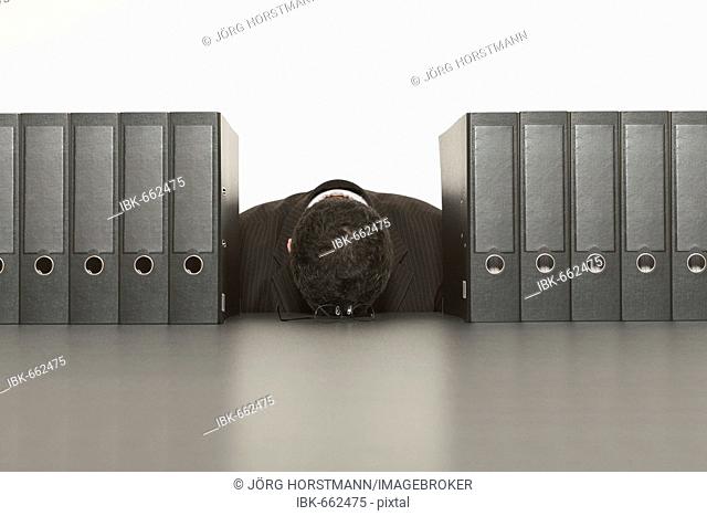 Businessman sleeping on desk surrounded by files (binders)