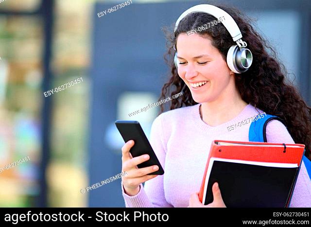 Happy student wearing headphones walks listening audio on phone