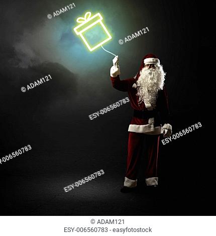 Santa Claus is holding a shining symbol of the gift on a string