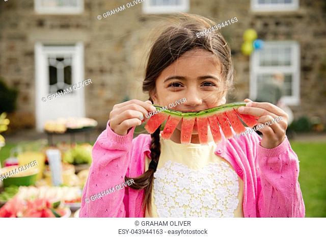 One young girl looking at the camera while holding a slice of watermelon as a smile