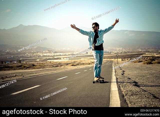 Adult young man moving on long board table on a long street asphalt road and outdoors mountains in background - concept of freedom and active people