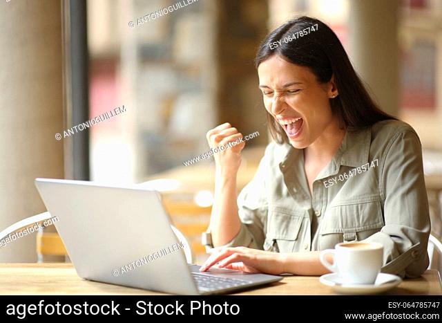 Excited woman celebrating good news in a restaurant checking laptop