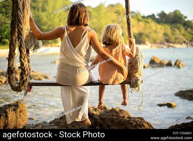 Mother and daughter on large rope swing over ocean, Thailand