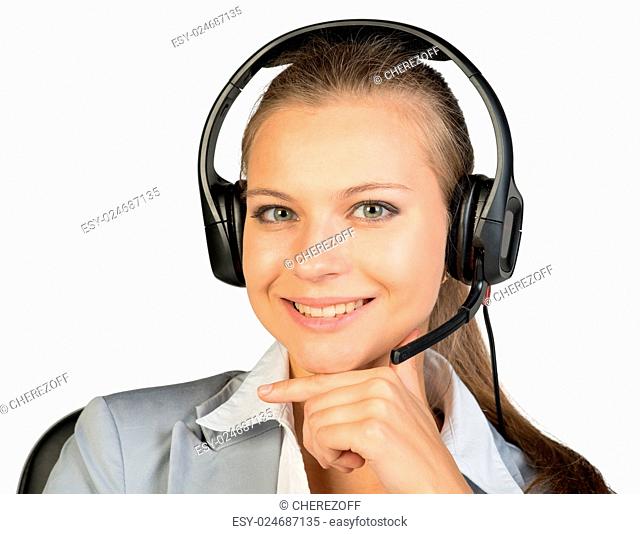 Businesswoman in headset sitting on chair, hand under chin, looking at camera, smiling. Isolated over white background