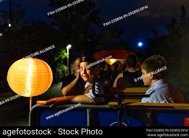 05 August 2022, Brandenburg, Cottbus: A youthful train conductor and passengers sit in a carriage during the so-called light rides of the Cottbus park railroad