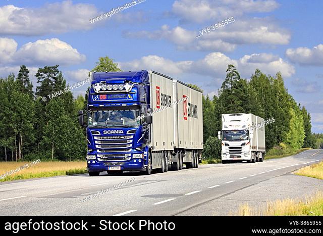 Two Scania freight transport trucks, blue DB Schenker in the foreground, haul goods along Highway 10 in the summer. Jokioinen, Finland. August 7, 2020