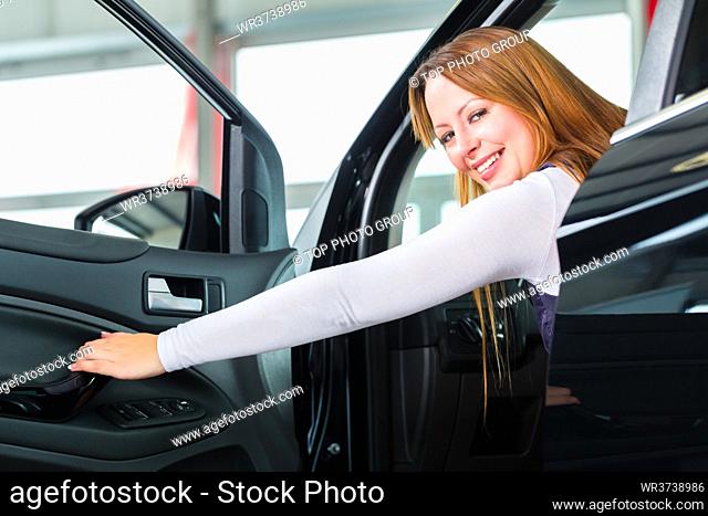 Young woman sits in new car on driver seat in a car dealership, obviously she is buying the auto