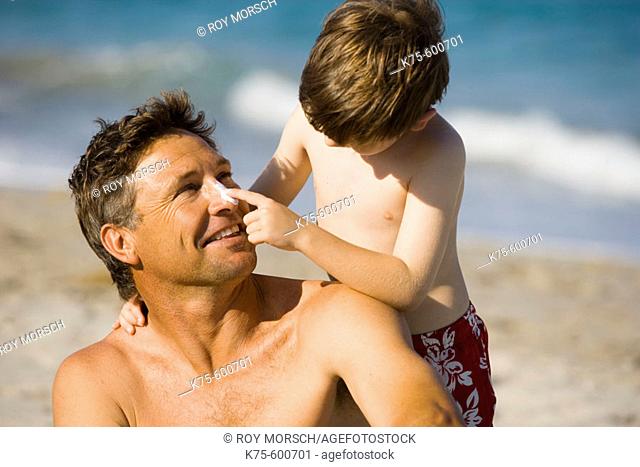 Son putting sunscreen on dad's nose