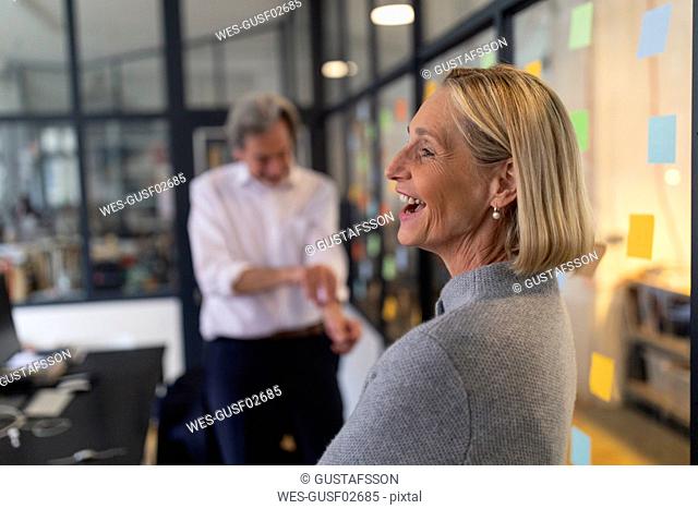 Happy businesswoman with colleague and sticky notes at glass pane in office