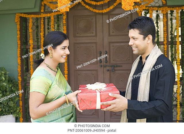 Side profile of a mid adult man giving a gift box to a young woman
