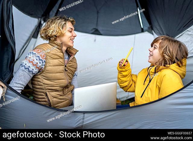 Two brothers camping inside tent with laptop and smart phone