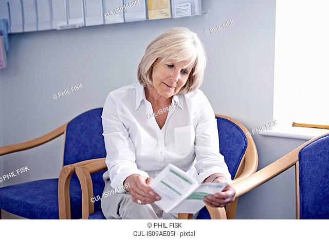 Mature female patient reading leaflet in hospital waiting room