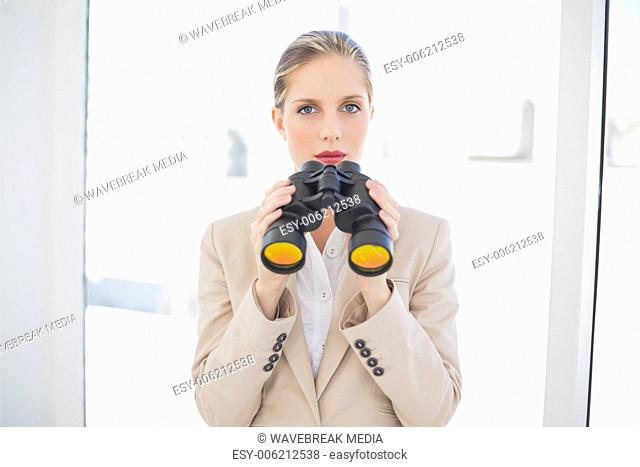Serious blonde businesswoman holding binoculars