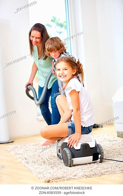 Mutter und Kinder haben Spaß im Haushalt beim Saubermachen mit Staubsauger