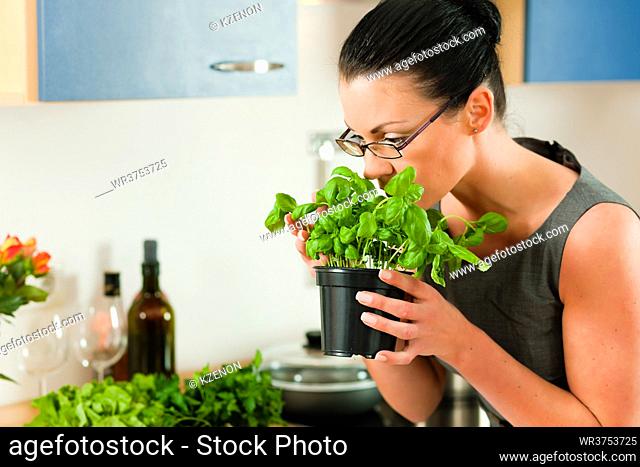 Woman smells the aroma of a basil pot in her kitchen