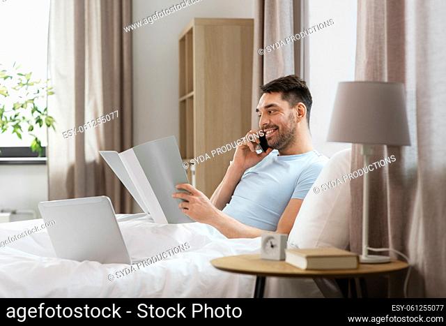 man with folder calling on phone in bed at home