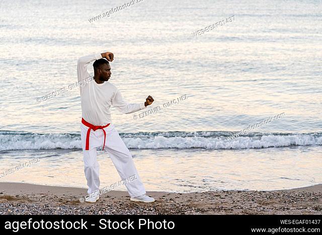 Adult man practicing martial arts on sandy coastal beach