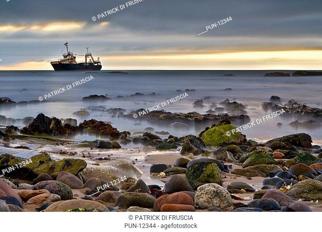An old abandoned shipwreck ghost type ship at dusk located and complimented by colourful rocks along the coast